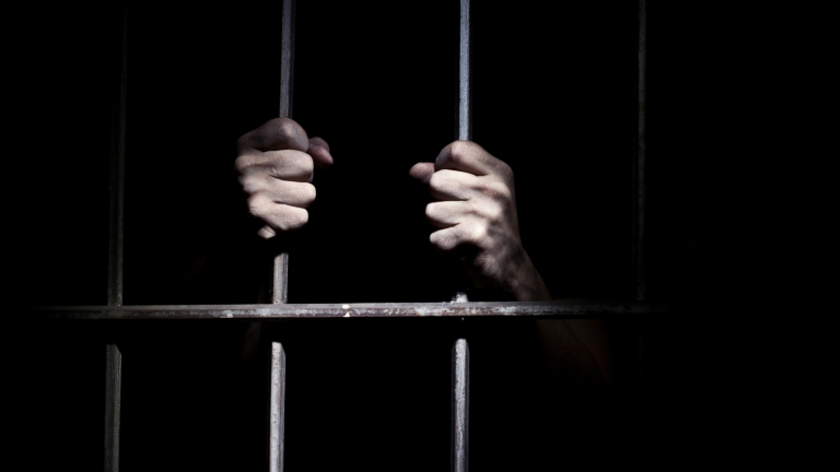 man's hands on prison bars