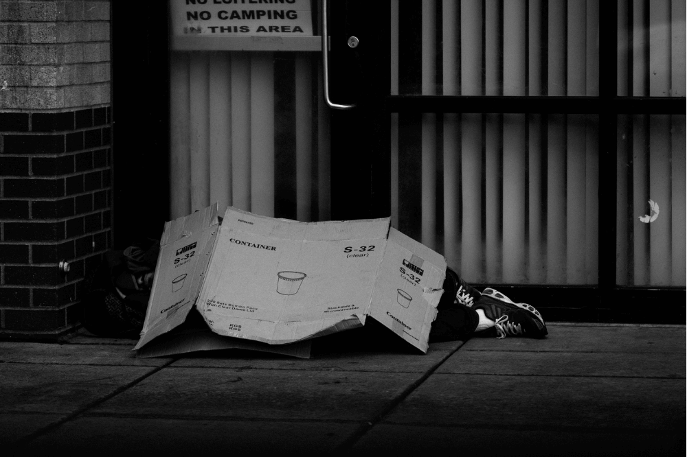 homeless person sleeping on the street with a cardboard blanket