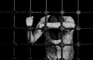 blac and white image of boy with hat behind bars looking down 