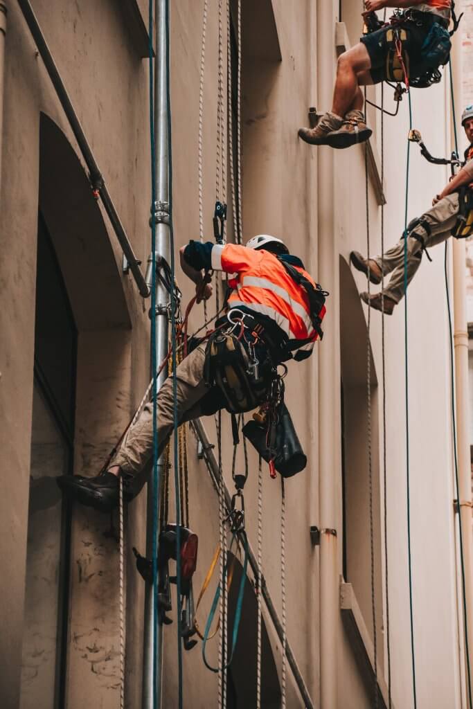 three construction/builders on the side of a beige wall doing work