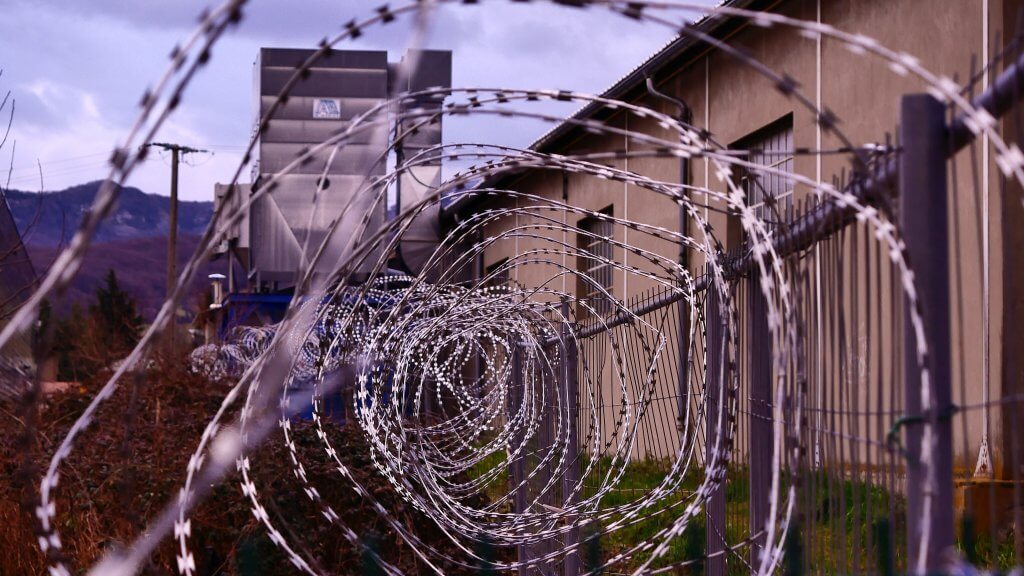 photo taken within barbed wire, can see directly within the circle of barbed wire with prison in background