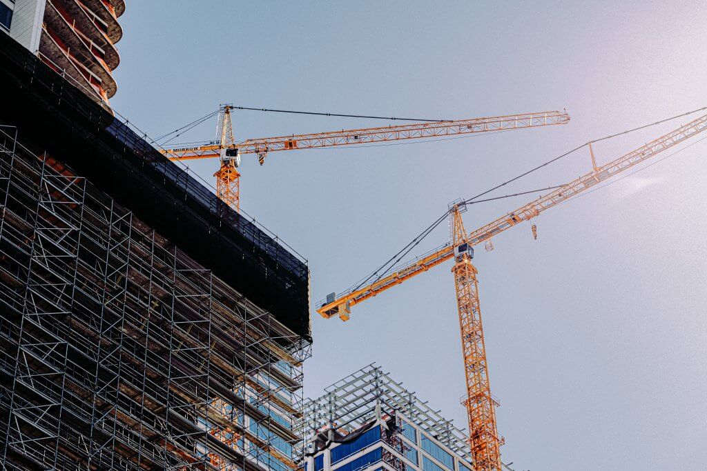 photo taken from the ground up to look up at building scaffolding with two yellow cranes and clear blue sky