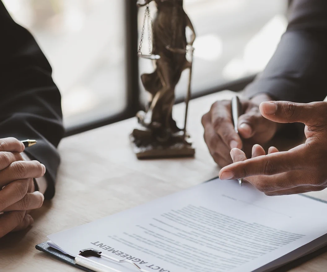 Esther Rockett defamation lawyers | O'BRIEN CRIMINAL & CIVIL SOLICITORS Two people discussing a document at a desk with a small statue of Lady Justice in the background. One hand points at a clause on the document, emphasizing details during a legal consultation.