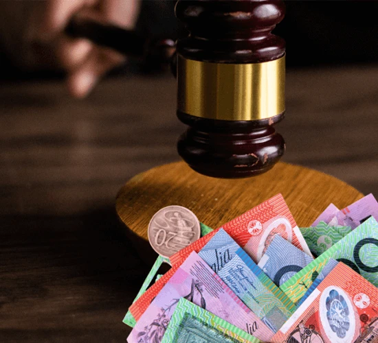 bail | O'BRIEN CRIMINAL & CIVIL SOLICITORS A judge's gavel with a brass band hits a wooden block on a dark brown table. In front of the block are various colorful Australian banknotes and a single Australian two-dollar coin.