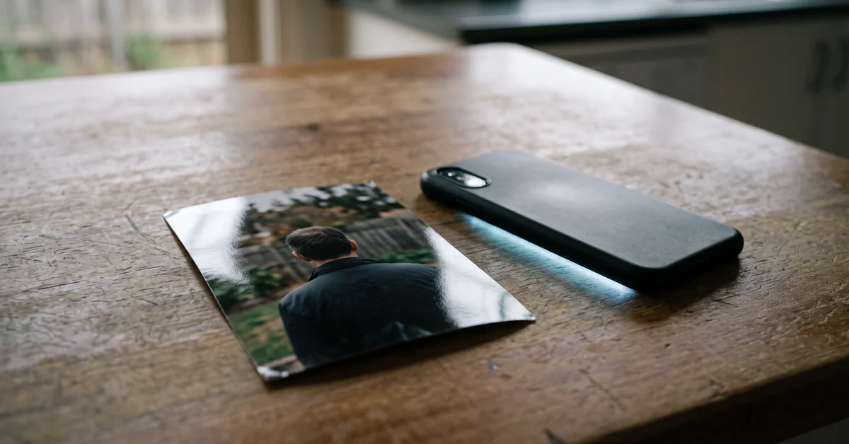 Small photographic print of a man seen from behind on a kitchen table beside a face-down phone