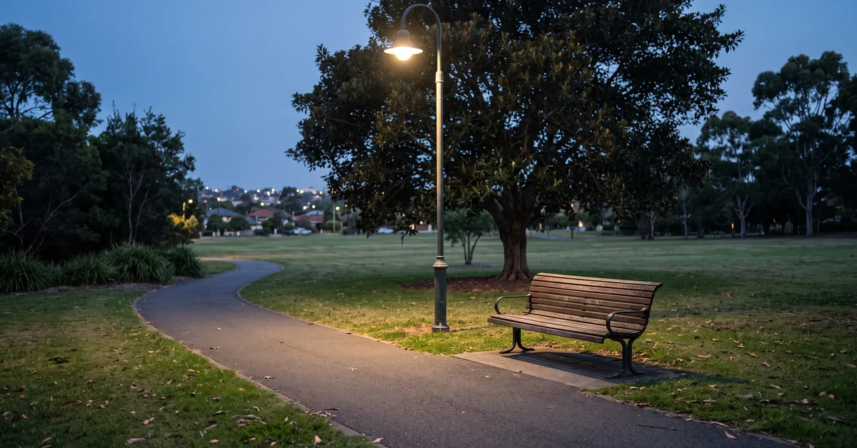Empty park bench beneath a streetlight at dusk