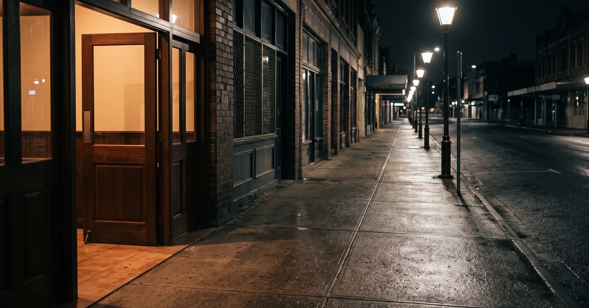 Empty footpath leading away from a lit bar entrance at night