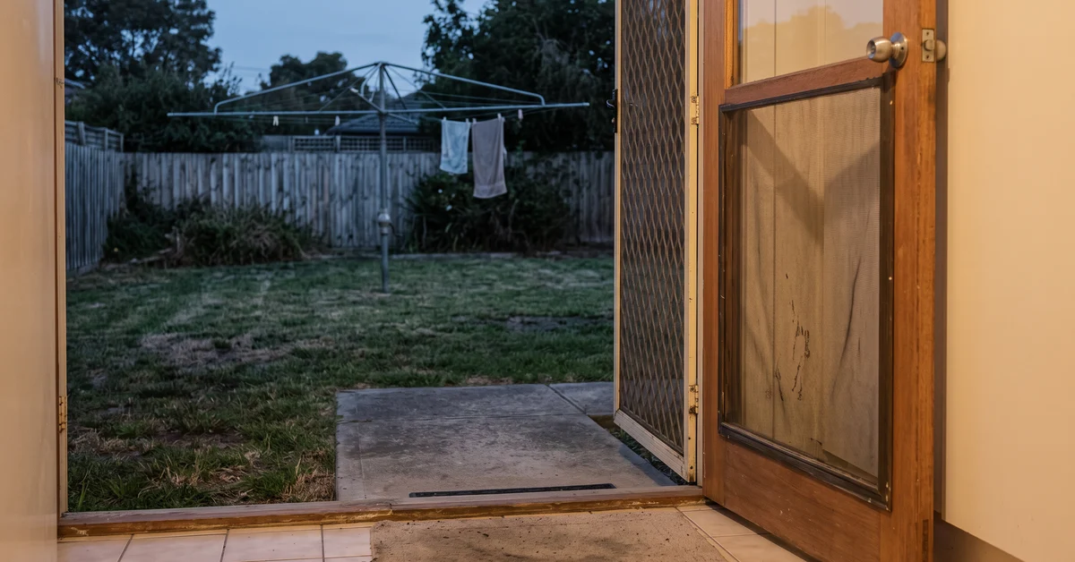Back screen door standing open onto a suburban backyard at dusk