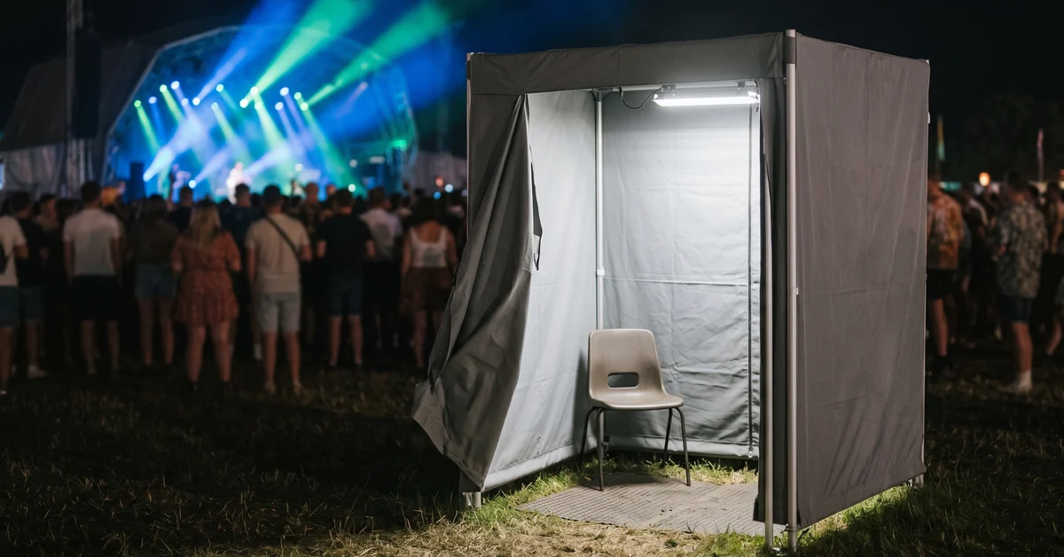 Screened search cubicle at a night music festival with stage lights beyond