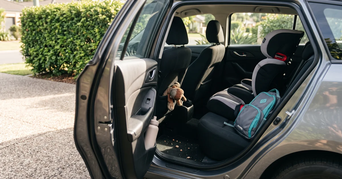 Child's booster seat and school bag in the back of a car on a sunny morning