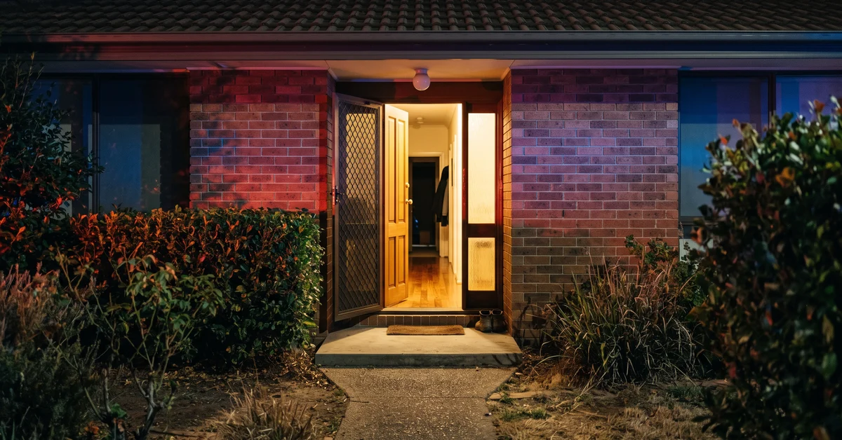 Open front door of a suburban Sydney home at night with emergency light on the wall