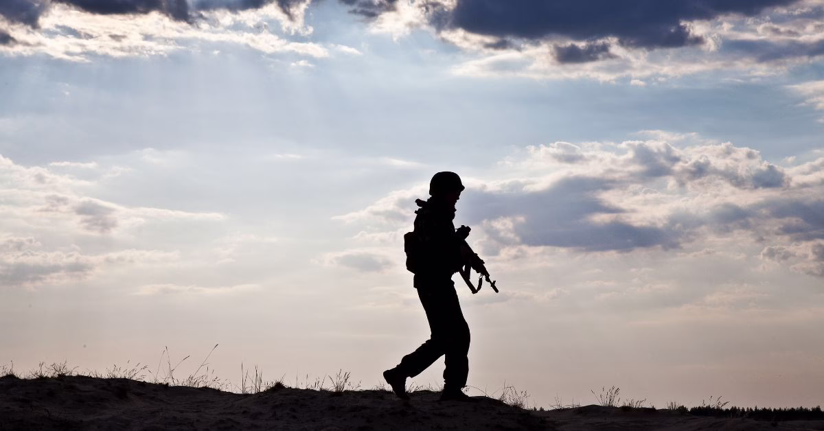 a soldier walks along a hill carrying a weapon