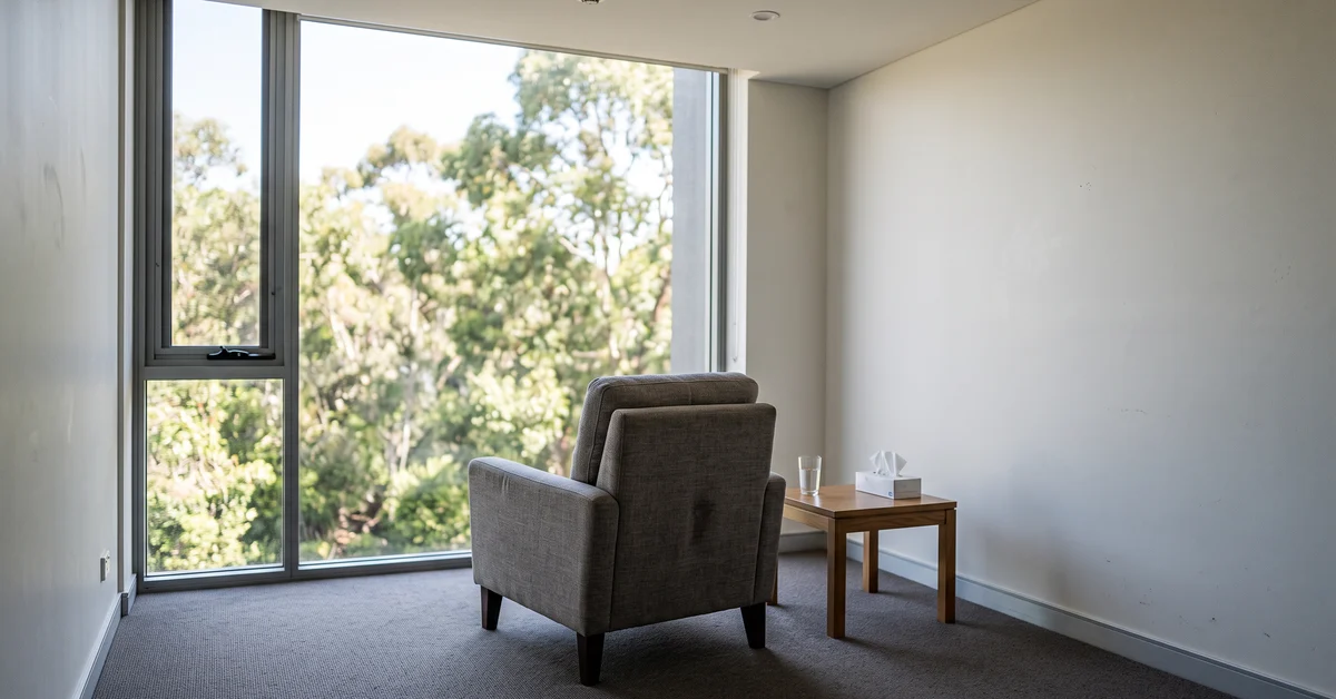 Single chair facing a bright window in a plain private room