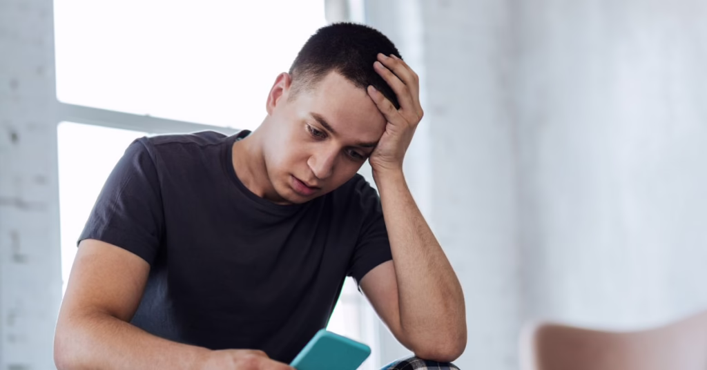 man looking at mobile phone in his hand with a distressed expression